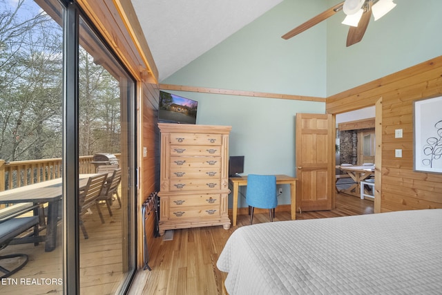 bedroom with light wood-style floors, ceiling fan, wooden walls, and high vaulted ceiling