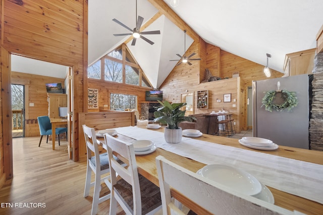 dining room with wooden walls, a ceiling fan, high vaulted ceiling, and light wood-style floors