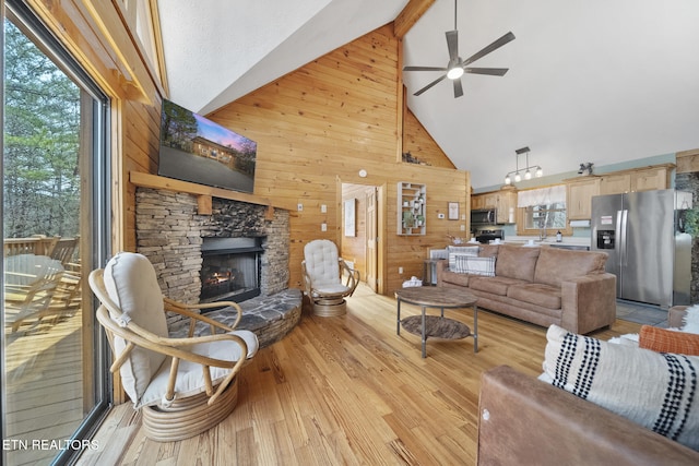 living room featuring wooden walls, high vaulted ceiling, a fireplace, and a ceiling fan