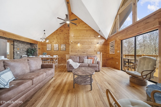 living room with light wood finished floors, ceiling fan with notable chandelier, wooden walls, and high vaulted ceiling