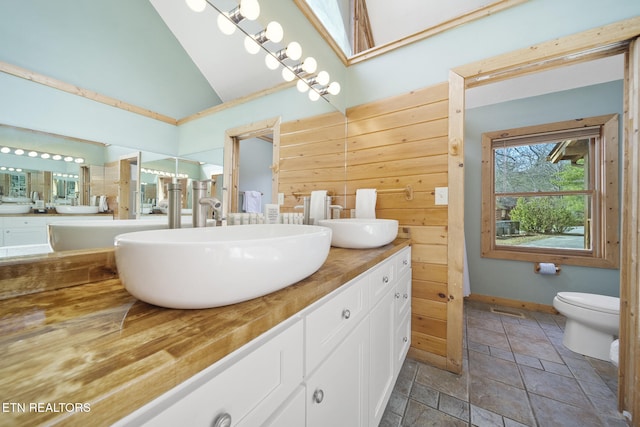 full bathroom with double vanity, a sink, vaulted ceiling, and toilet