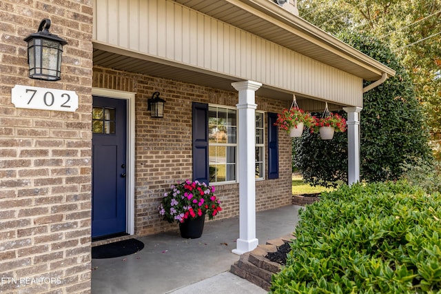 view of exterior entry with a porch and brick siding