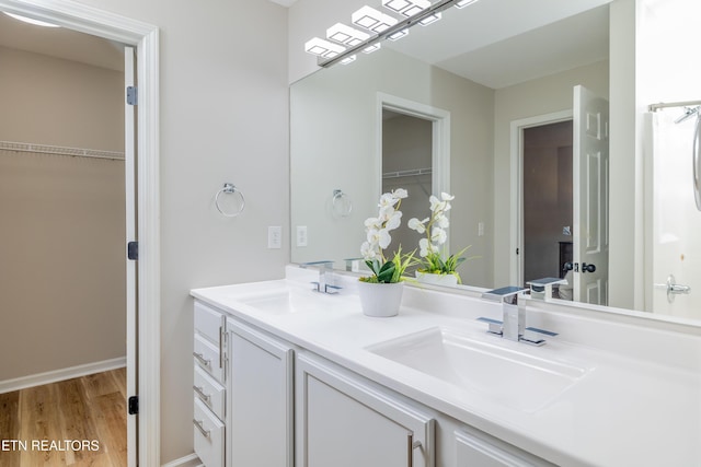 full bath with a sink, a walk in closet, double vanity, and wood finished floors