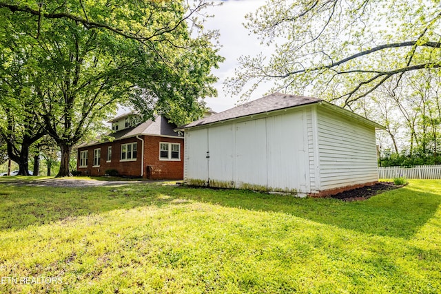 view of side of property with a yard, brick siding, fence, and an outdoor structure