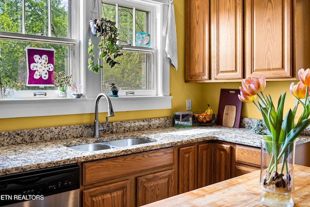 kitchen with stainless steel dishwasher, brown cabinets, light stone counters, and a sink