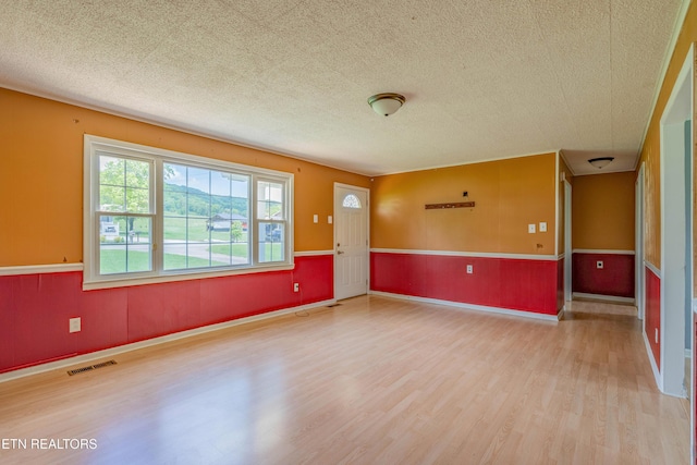 unfurnished room with a wainscoted wall, a textured ceiling, visible vents, and wood finished floors