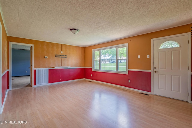 entrance foyer with a textured ceiling, visible vents, wood finished floors, and wainscoting