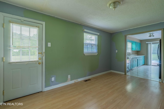 interior space with a textured ceiling, light wood-type flooring, plenty of natural light, and visible vents