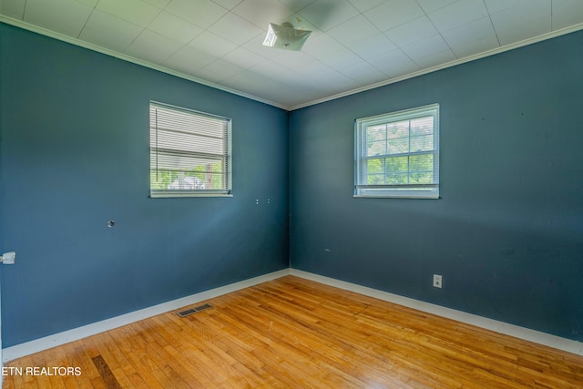 empty room with baseboards, ornamental molding, visible vents, and hardwood / wood-style flooring