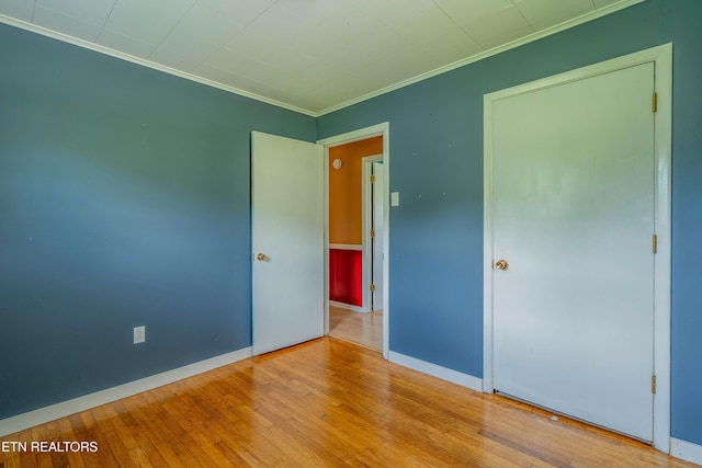unfurnished bedroom with wood finished floors, baseboards, and ornamental molding