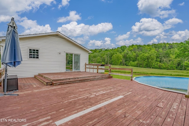 deck featuring an outdoor pool and a view of trees