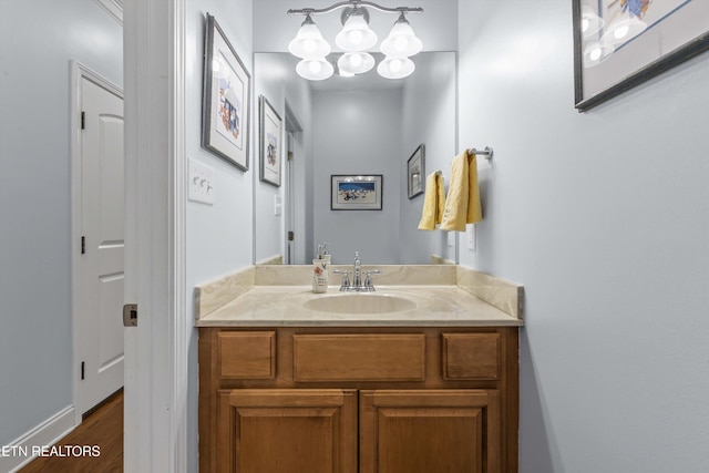 bathroom with baseboards, an inviting chandelier, wood finished floors, and vanity