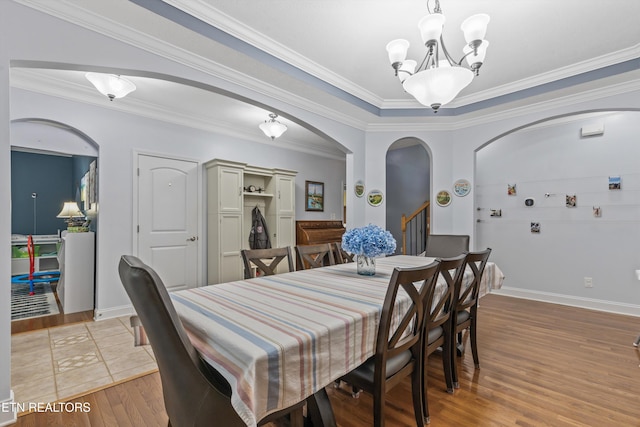 dining room with crown molding, a notable chandelier, light wood finished floors, arched walkways, and baseboards