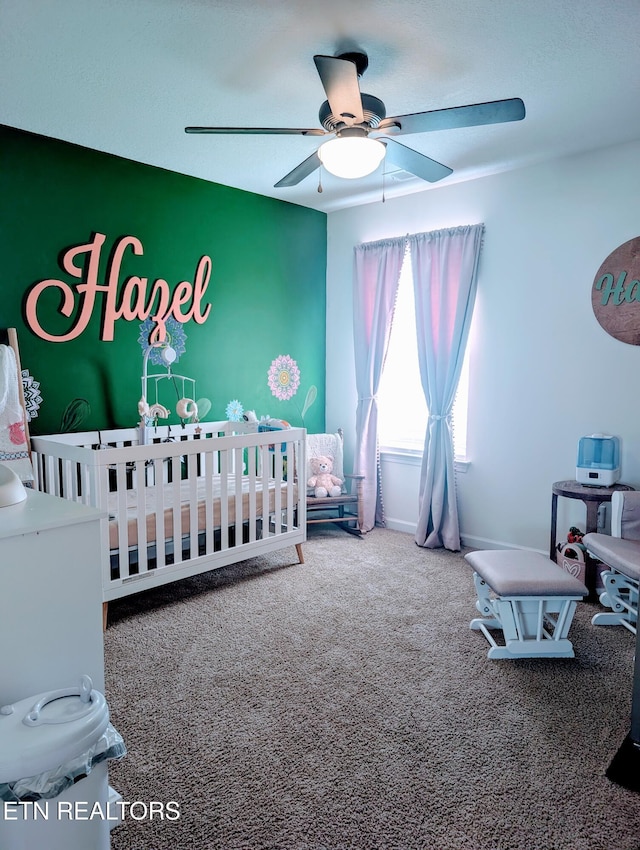 carpeted bedroom with ceiling fan and a crib