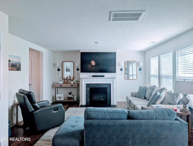 living area featuring wood finished floors, a fireplace with flush hearth, a textured ceiling, visible vents, and baseboards