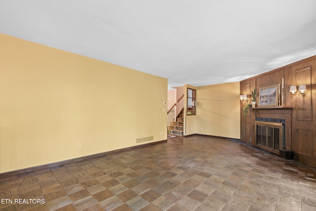 unfurnished living room featuring visible vents, stairs, a glass covered fireplace, and baseboards