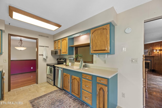 kitchen featuring appliances with stainless steel finishes, a sink, light countertops, brown cabinetry, and baseboards