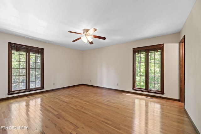 spare room with wood-type flooring, a ceiling fan, baseboards, and visible vents