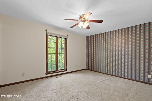 carpeted empty room with a ceiling fan, baseboards, visible vents, and wallpapered walls