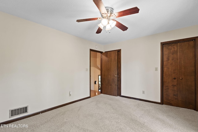 unfurnished bedroom featuring a ceiling fan, visible vents, carpet floors, baseboards, and multiple closets