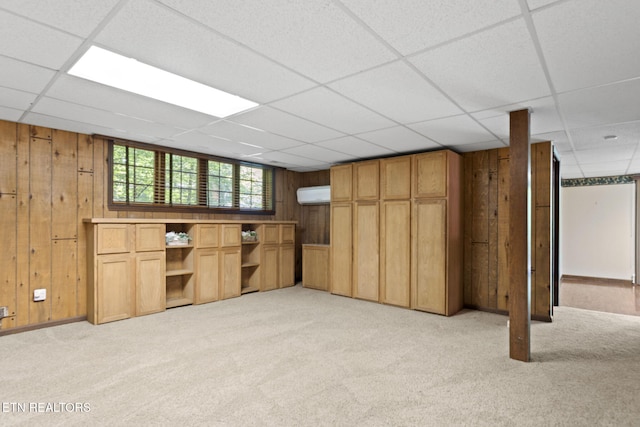 basement with wooden walls, light carpet, an AC wall unit, and a drop ceiling