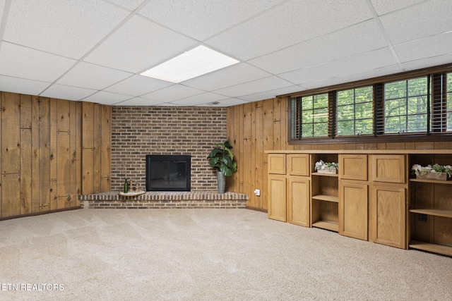 unfurnished living room featuring wooden walls, carpet floors, a brick fireplace, and a paneled ceiling