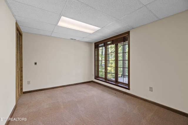 unfurnished room featuring baseboards, a drop ceiling, and carpet