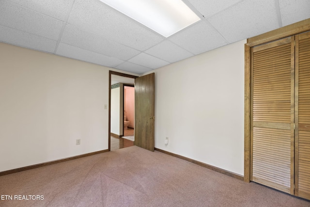 unfurnished bedroom featuring baseboards, carpet, a closet, and a drop ceiling