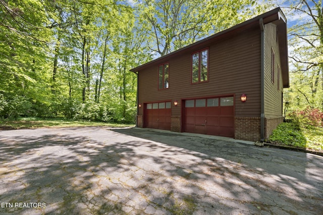 view of home's exterior with brick siding, a garage, and aphalt driveway