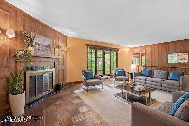 living room featuring baseboards, a glass covered fireplace, and wooden walls