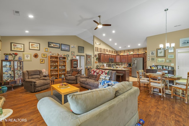 living area with visible vents, ceiling fan with notable chandelier, wood finished floors, and high vaulted ceiling