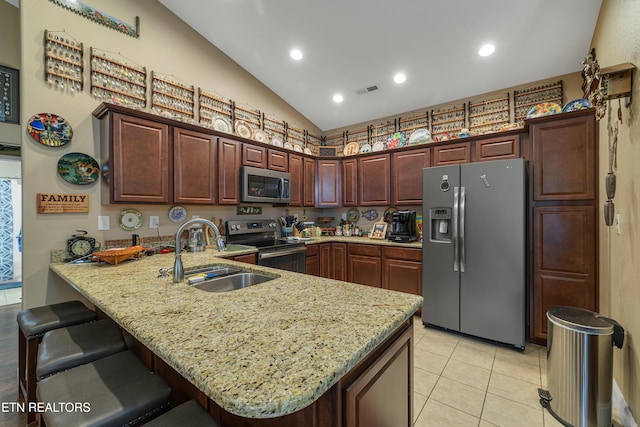 kitchen with light stone countertops, a sink, a peninsula, a breakfast bar, and stainless steel appliances