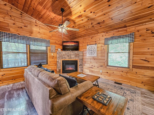 living area with wood finished floors, vaulted ceiling, wood walls, ceiling fan, and a fireplace