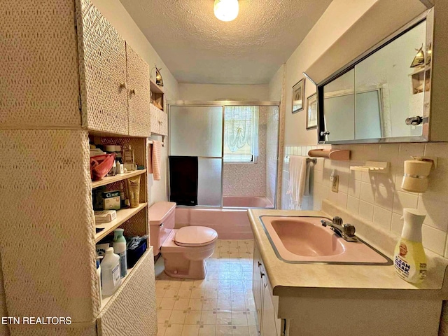 full bath featuring vanity, bath / shower combo with glass door, tile patterned floors, toilet, and a textured ceiling