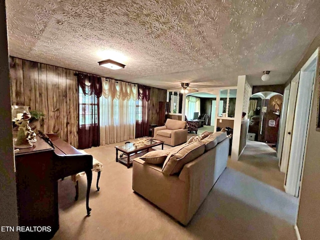living area featuring arched walkways, a textured ceiling, ceiling fan, carpet flooring, and wooden walls