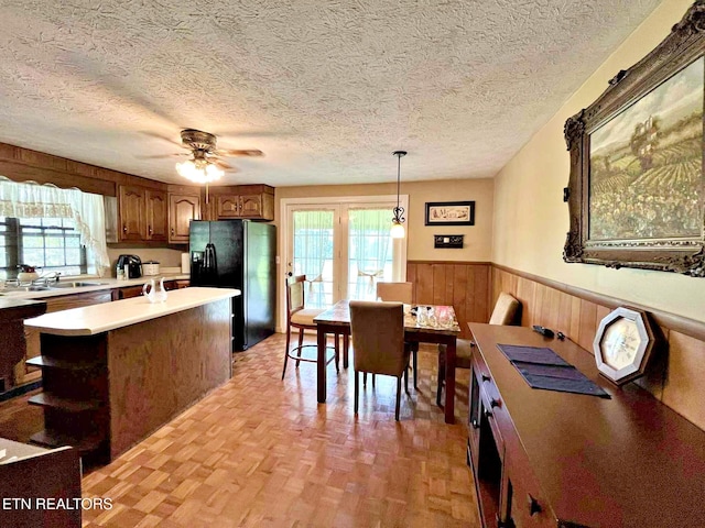 kitchen with light countertops, a wainscoted wall, a sink, a ceiling fan, and black fridge