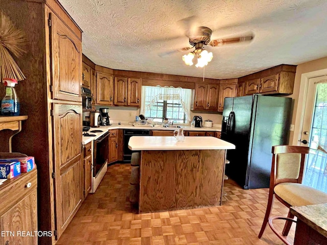 kitchen featuring black appliances, a ceiling fan, light countertops, and a healthy amount of sunlight