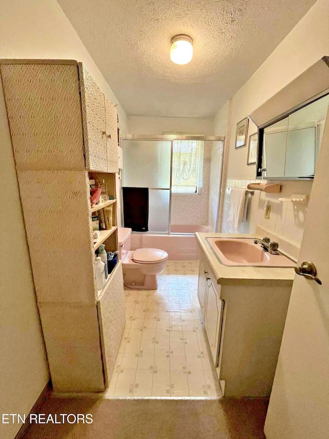 full bathroom featuring shower / bath combination with glass door, vanity, tile patterned floors, toilet, and a textured ceiling