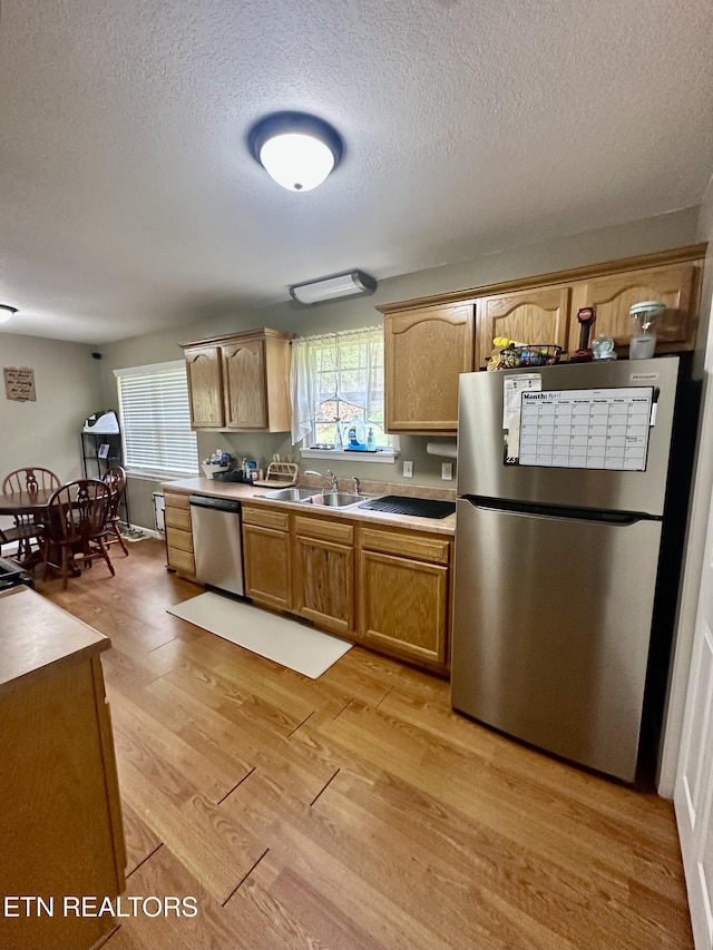 kitchen with a sink, a textured ceiling, appliances with stainless steel finishes, and light wood-style flooring