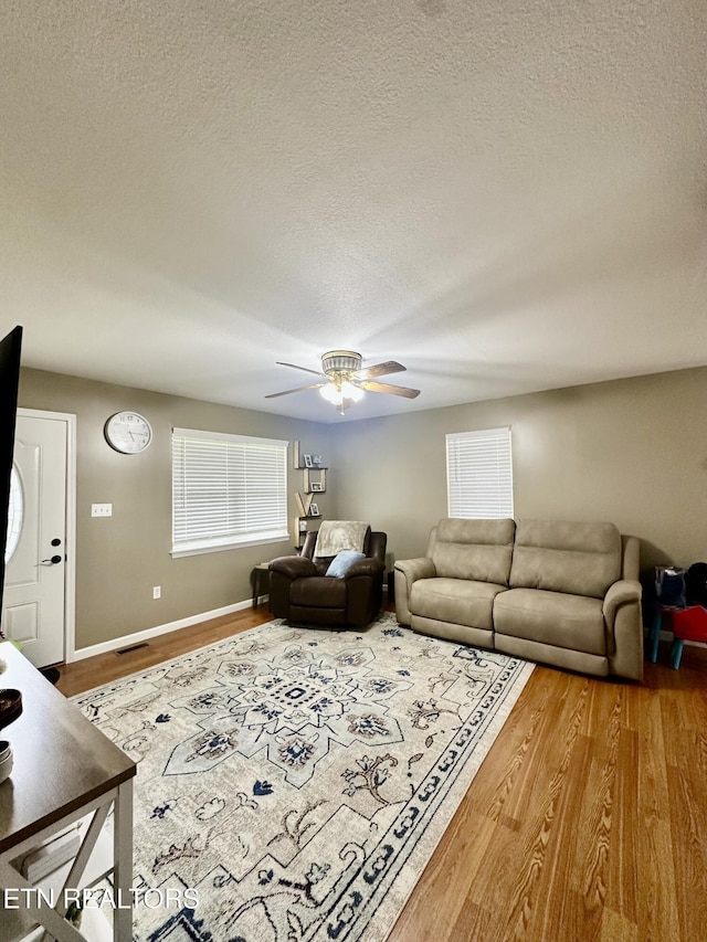 living area featuring a textured ceiling, ceiling fan, baseboards, and wood finished floors