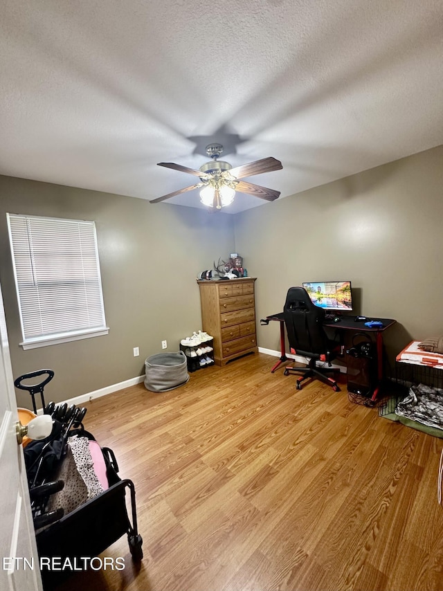 interior space with baseboards, a ceiling fan, light wood-type flooring, and a textured ceiling