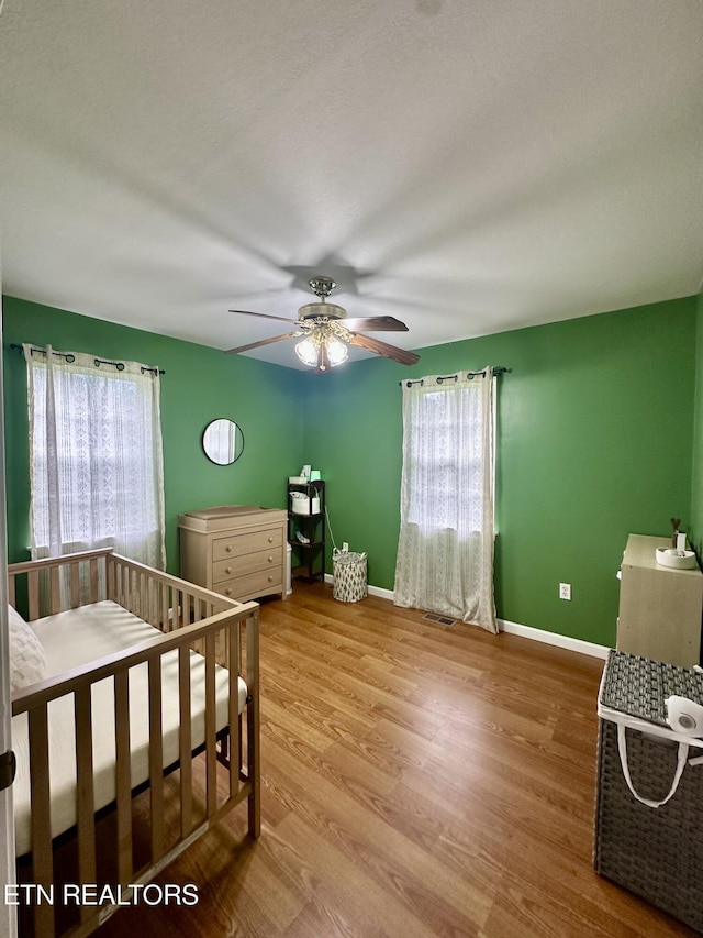bedroom featuring baseboards, ceiling fan, wood finished floors, and visible vents