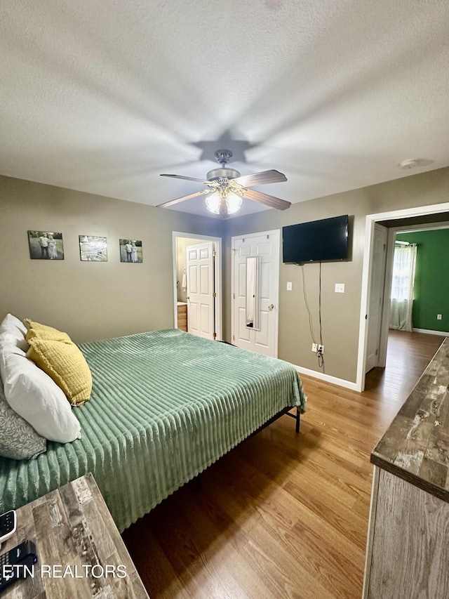 bedroom featuring baseboards, a ceiling fan, a textured ceiling, and wood finished floors
