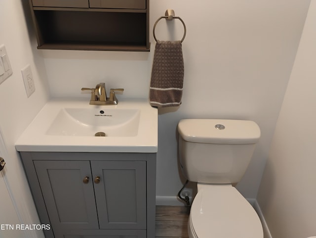 half bathroom featuring toilet, baseboards, and vanity