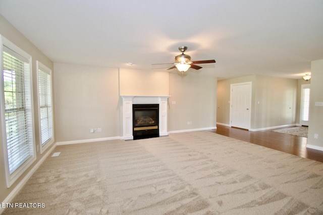 unfurnished living room with carpet floors, a ceiling fan, a fireplace with flush hearth, and baseboards