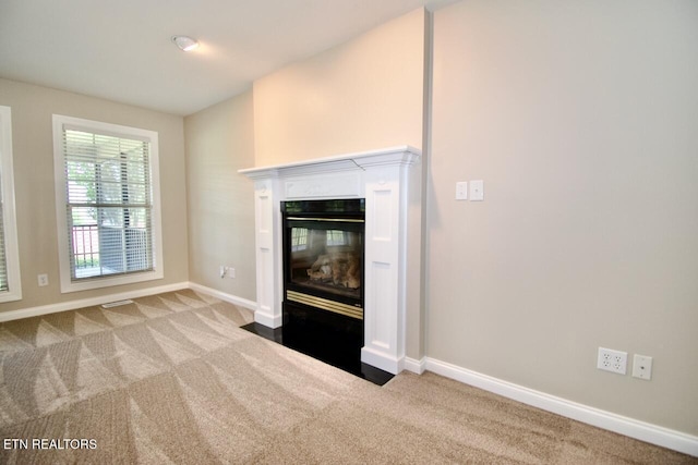 unfurnished living room featuring baseboards, a fireplace with flush hearth, and carpet