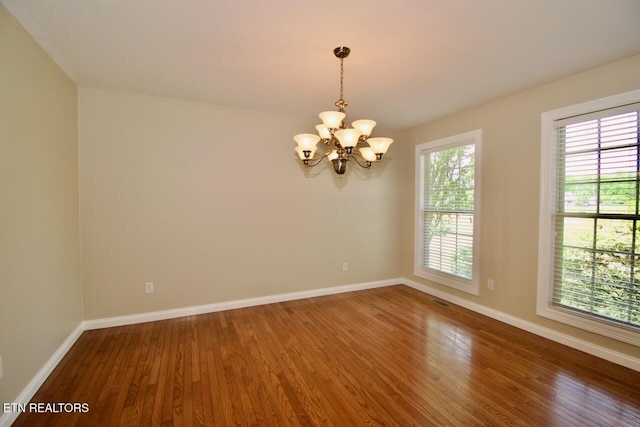 spare room with baseboards, wood finished floors, and a notable chandelier