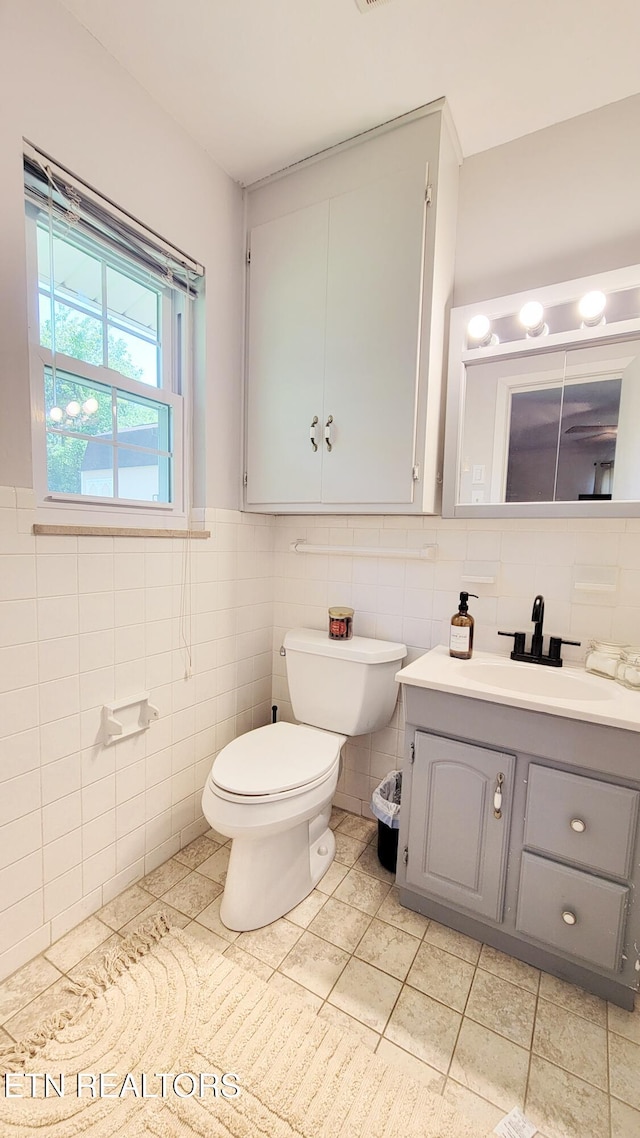 half bath featuring tile patterned flooring, vanity, toilet, and tile walls