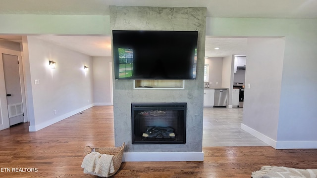 living area featuring visible vents, light wood-style flooring, baseboards, and a glass covered fireplace
