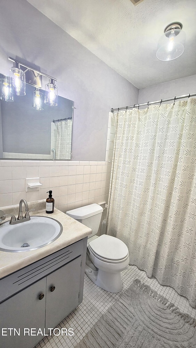 full bath with tile walls, vanity, a wainscoted wall, tile patterned floors, and toilet
